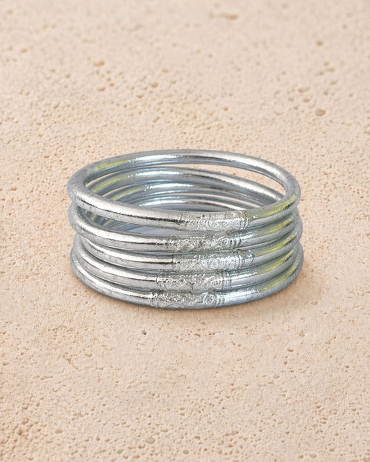 Accumulation de 5 joncs bouddhistes argent Bâan Kumlaï avec feuilles d’argent visibles sur fond minéral chaud
