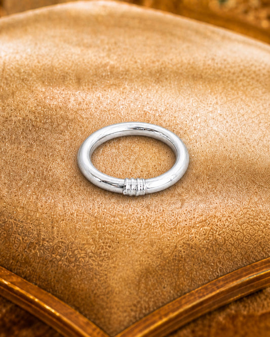 Détail d’une bague bouddhiste argent Bâan Kumlaï posée sur coussin beige, avec finition argent brillante.