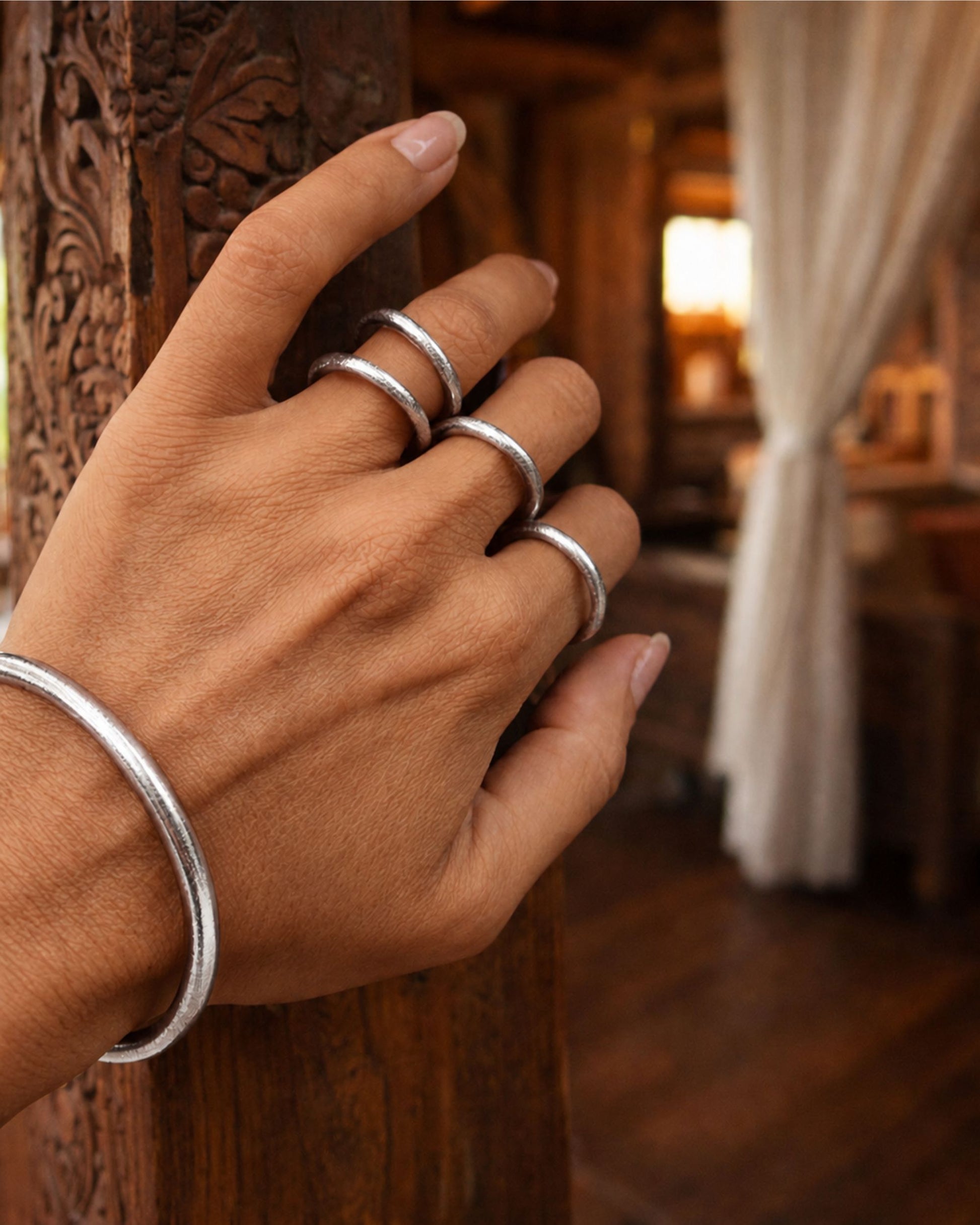 Bagues bouddhistes argent Bâan Kumlaï portées à la main, dans un décor en bois sculpté chaleureux