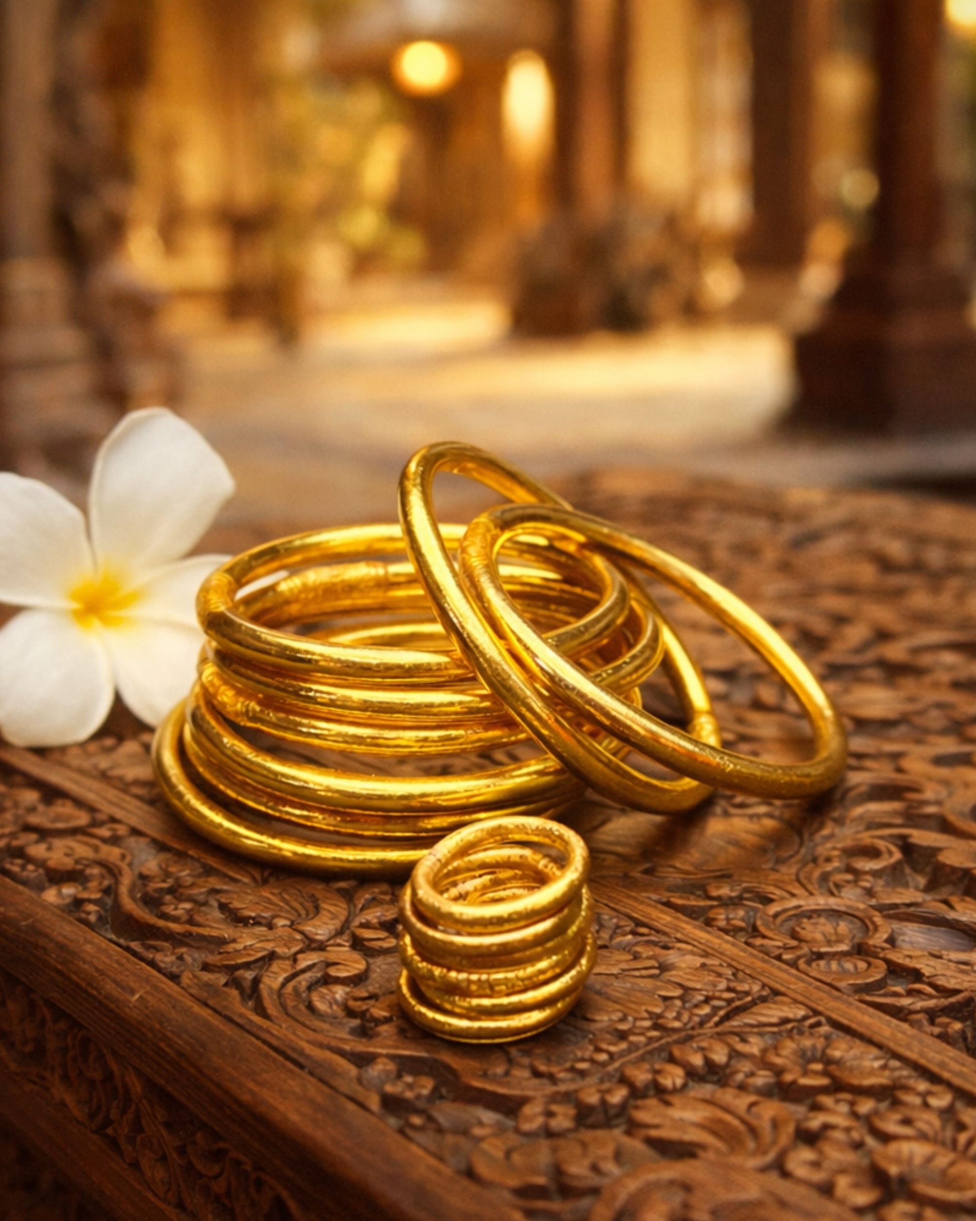 Bague bouddhiste or Bâan Kumlaï présentée avec bracelets Kumlaï dorés assortis et fleur blanche sur bois sculpté