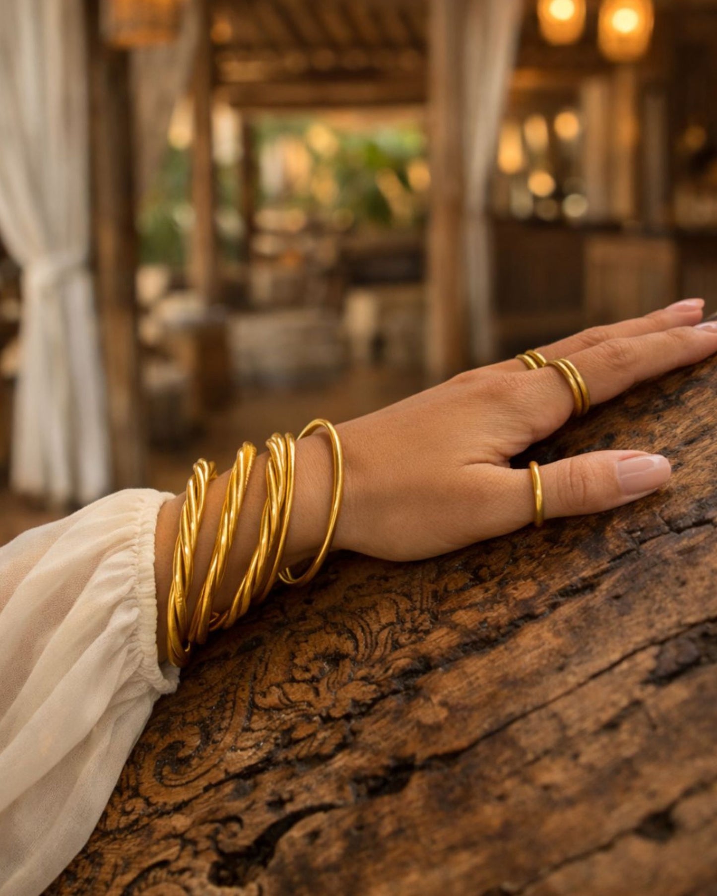Bague bouddhiste or Bâan Kumlaï portée avec bracelet Kumlaï doré sur main posée sur une rampe en bois sculpté