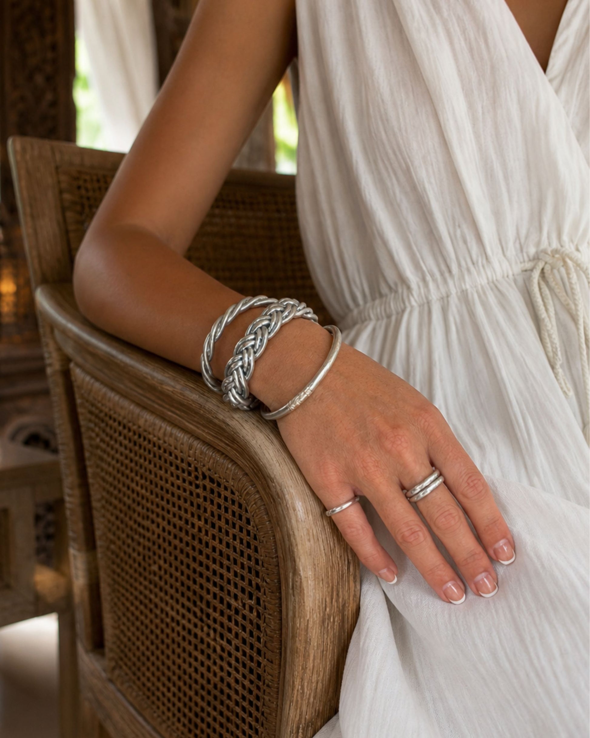 Bague Kumlai argent portée avec bracelet bouddhiste argent Bâan Kumlaï, sur une femme assise dans un décor chaleureux