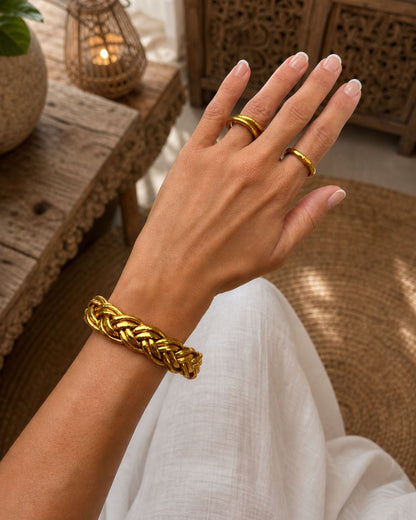 Bracelet Kumlai or tressé porté au poignet avec bagues dorées assorties, dans un style élégant et féminin.