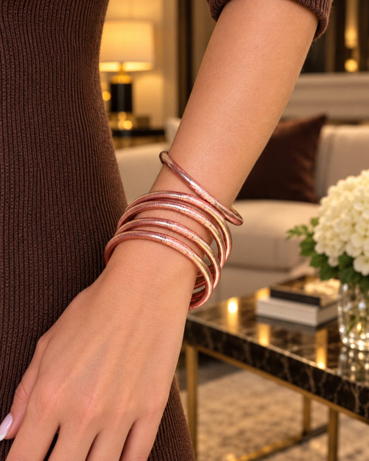 Bracelets bouddhistes Rose Poudré avec mantra gravé, portés au poignet avec un pull marron dans un salon élégant.