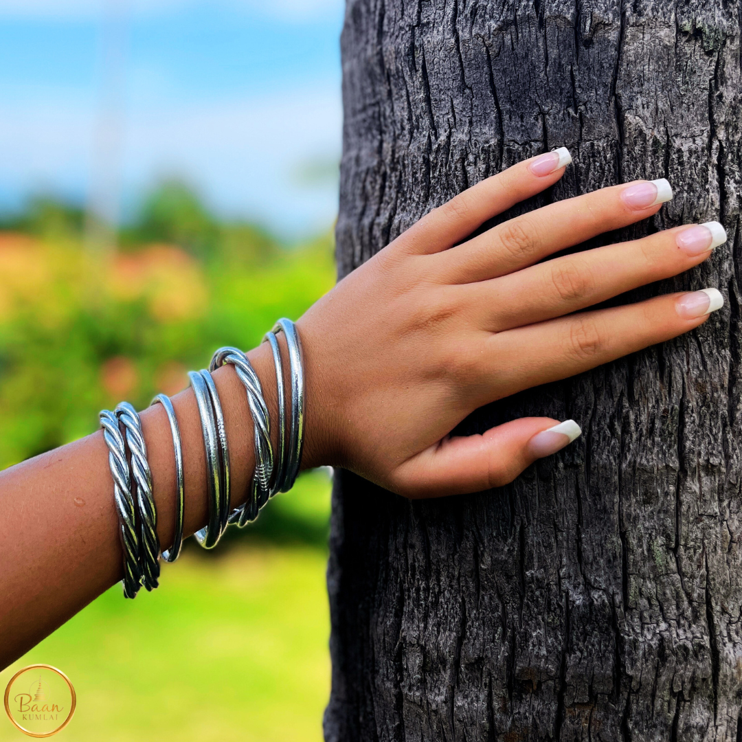 Poignet portant huit joncs bouddhistes Bâan Kumlaï en argent, mélange de joncs fins et torsadés