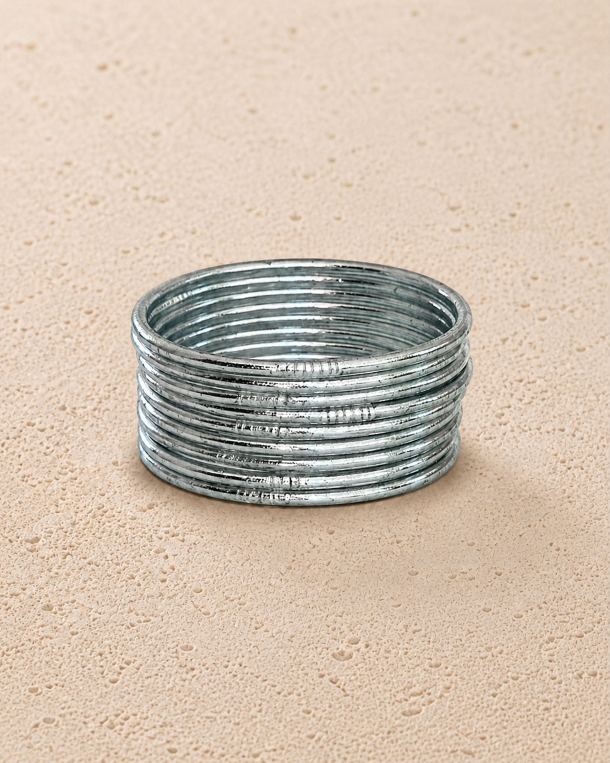 Accumulation de joncs bouddhistes argent fins Bâan Kumlaï sur fond minéral chaud, Kumlai argent fabriqués en Thaïlande
