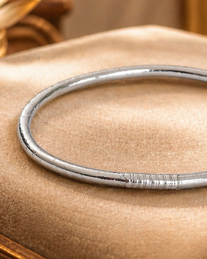 Détail du jonc bouddhiste argent fin Bâan Kumlaï avec finition argentée brillante sur coussin beige premium
