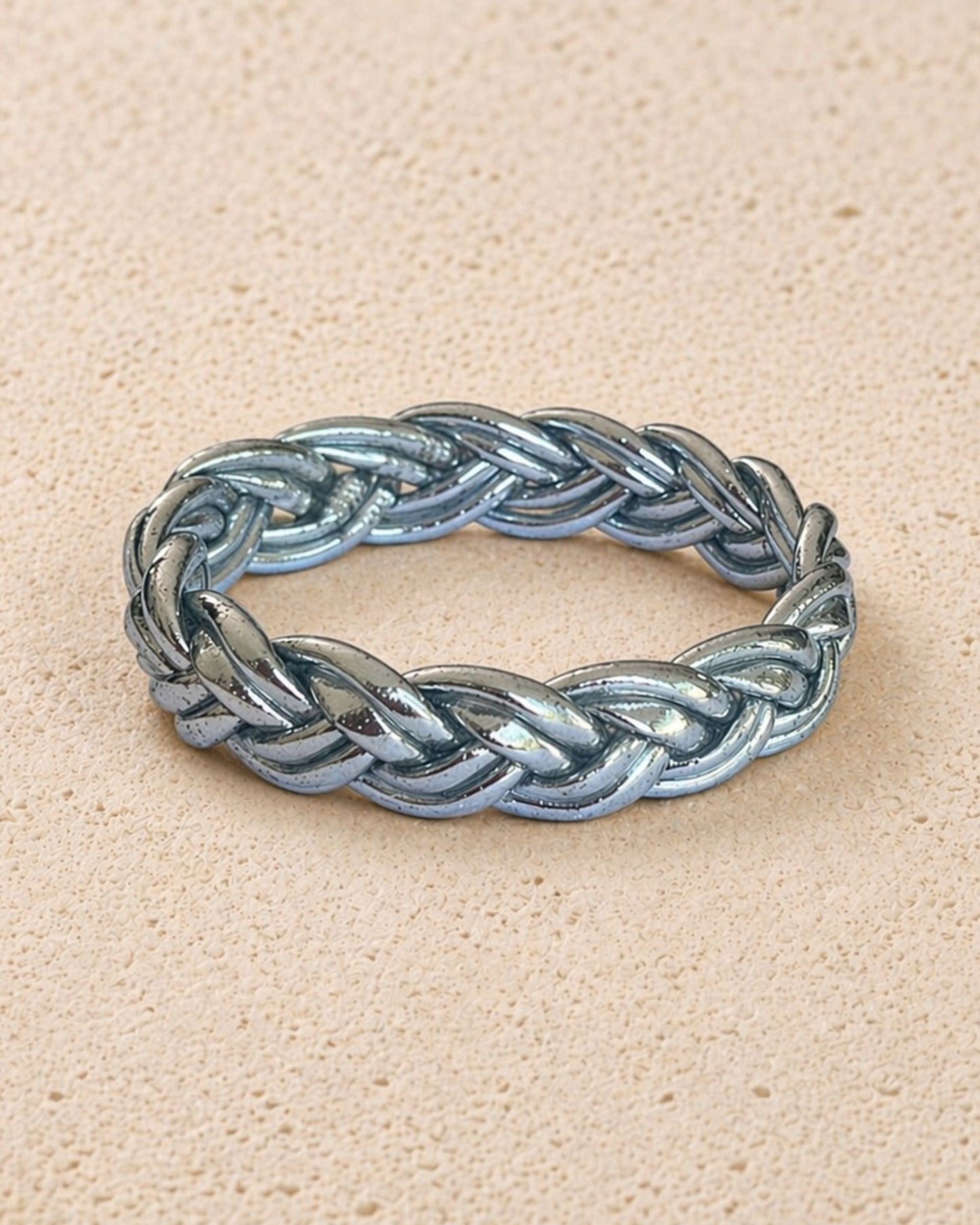 Jonc bouddhiste argent tressé Bâan Kumlaï, bracelet Kumlai argent présenté seul sur fond minéral chaud.