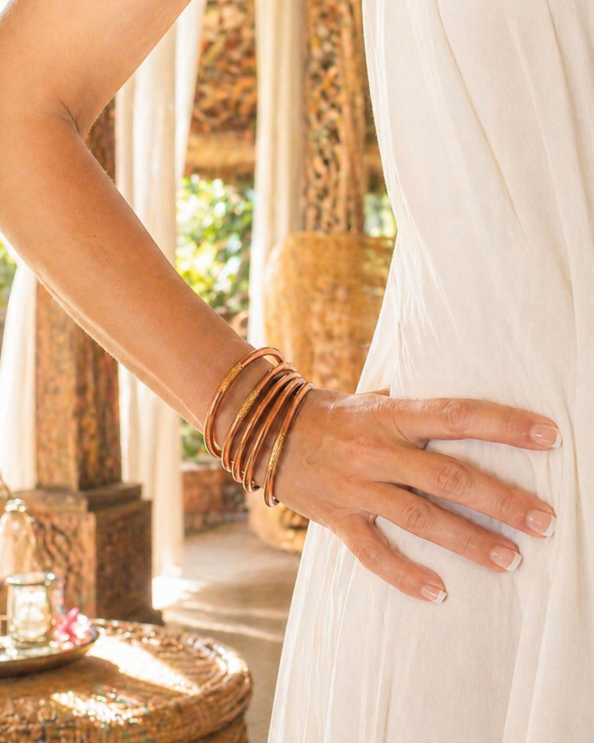 Joncs bouddhistes cuivre Bâan Kumlaï portés au poignet avec robe blanche dans une ambiance chaleureuse