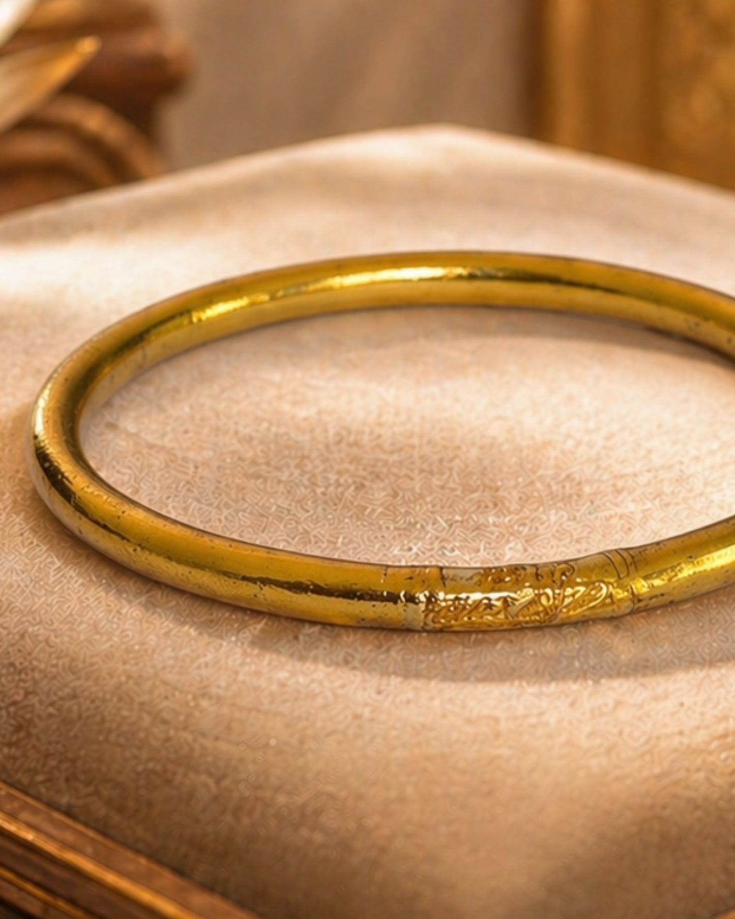 Détail du jonc bouddhiste or antique Bâan Kumlaï avec mantra gravé et feuilles d'or, bracelet Kumlai or antique sur coussin beige
