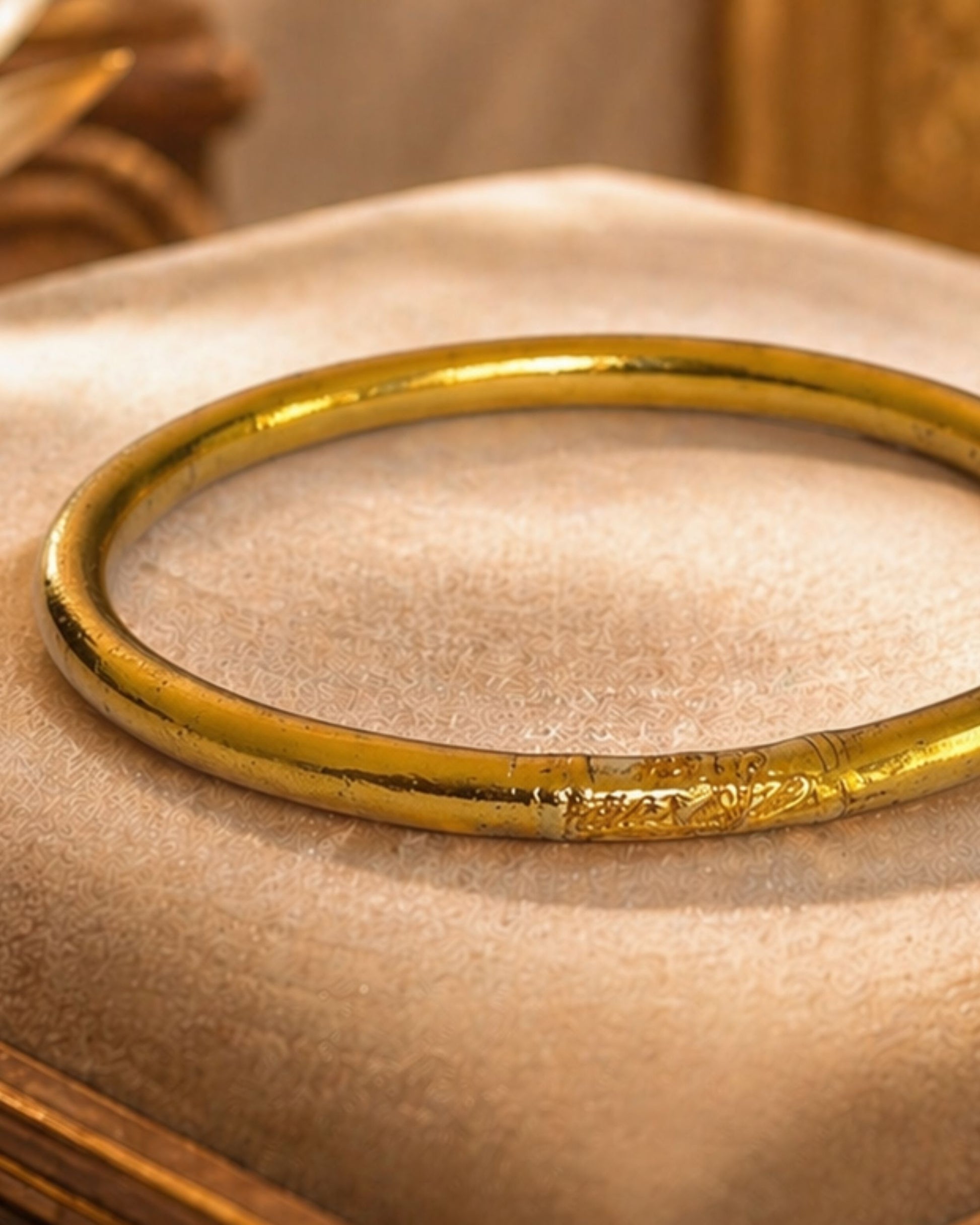 Détail du jonc bouddhiste or antique Bâan Kumlaï avec mantra gravé et feuilles d'or, bracelet Kumlai or antique sur coussin beige