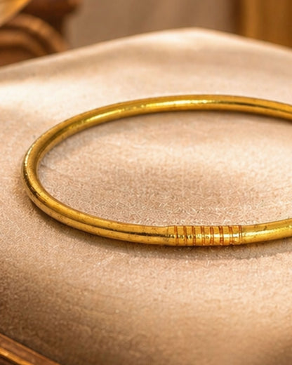 Détail du bracelet jonc bouddhiste or fin Bâan Kumlaï avec fermoir doré et finition brillante sur textile beige premium