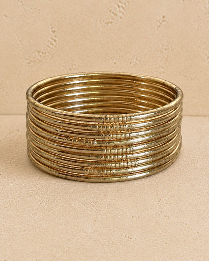 Accumulation de 9 joncs bouddhistes or rose fins Bâan Kumlaï sur fond minéral chaud, bracelet kumlai fin élégant fabriqué en Thaïlande.