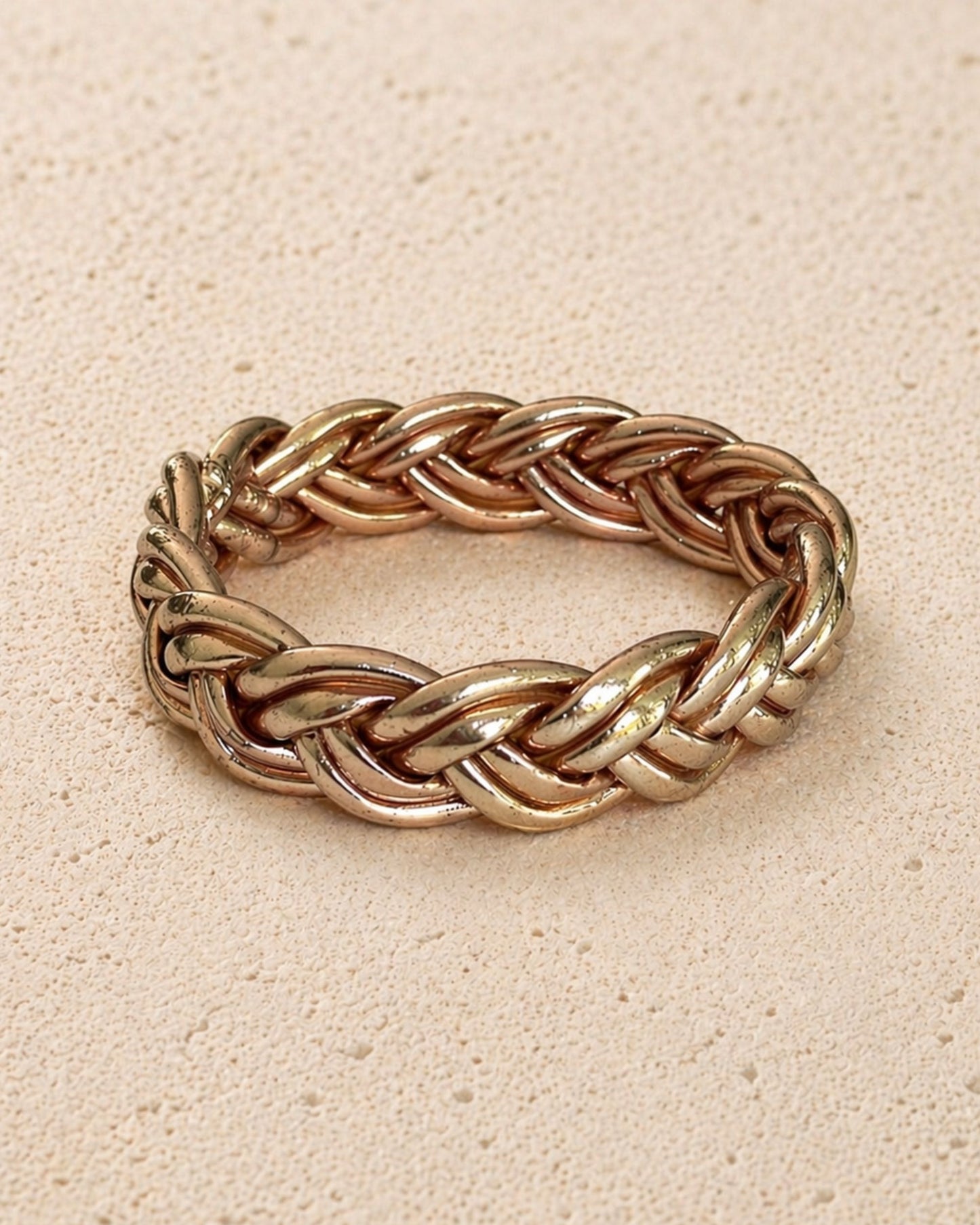 Jonc bouddhiste or rose tressé Bâan Kumlaï, bracelet Kumlai or rose présenté seul sur fond minéral chaud