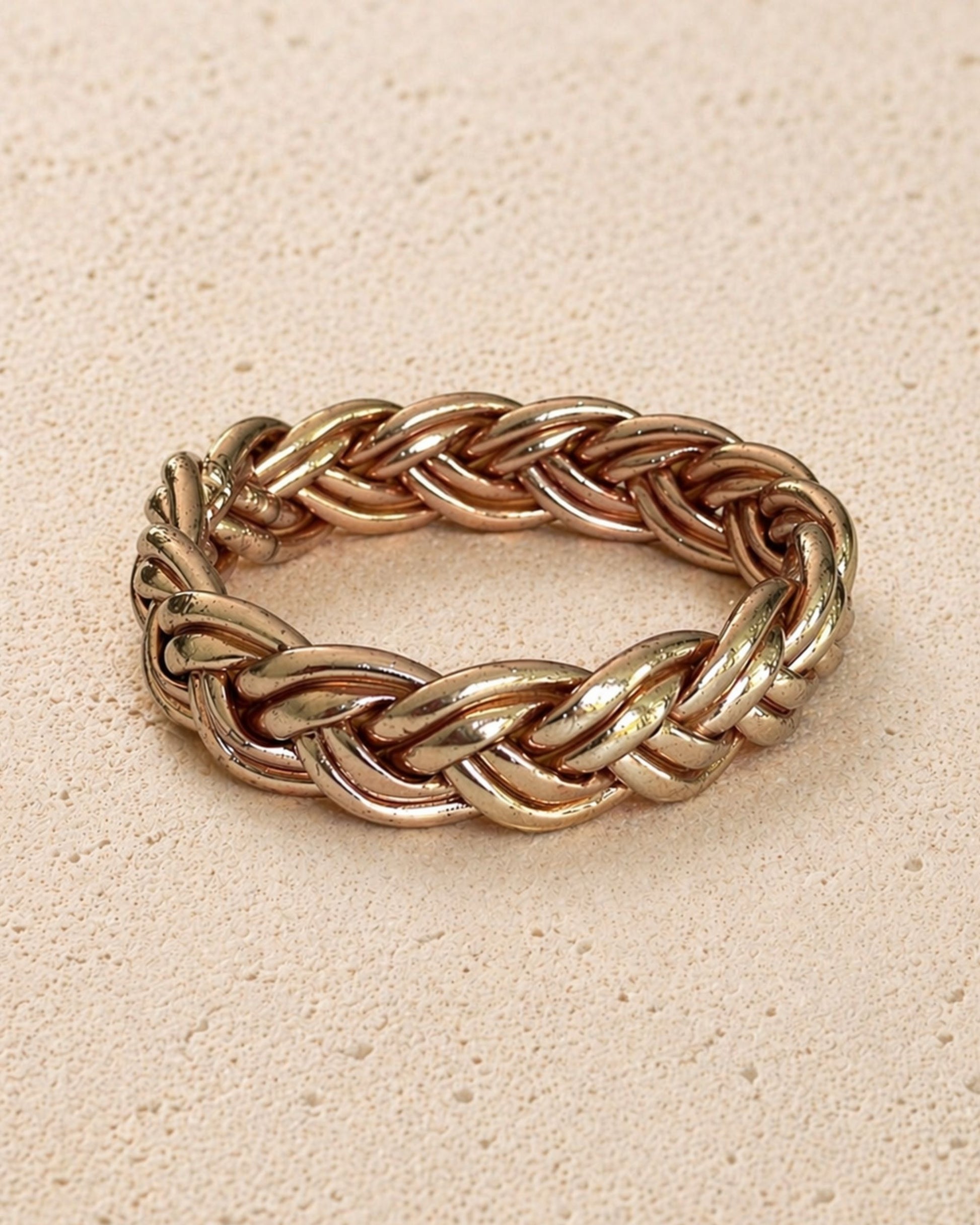 Jonc bouddhiste or rose tressé Bâan Kumlaï, bracelet Kumlai or rose présenté seul sur fond minéral chaud