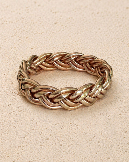 Jonc bouddhiste or rose tressé Bâan Kumlaï, bracelet Kumlai or rose présenté seul sur fond minéral chaud