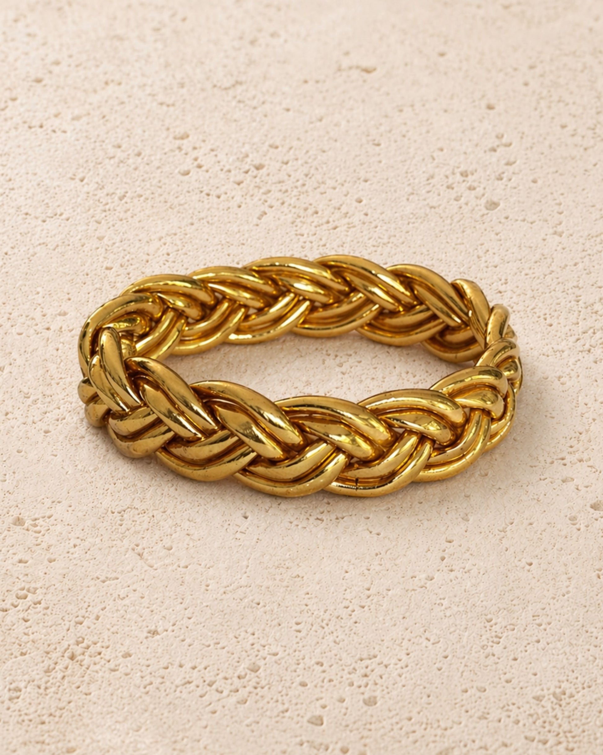 Jonc bouddhiste or tressé Bâan Kumlaï, bracelet Kumlai doré présenté seul sur fond minéral chaud