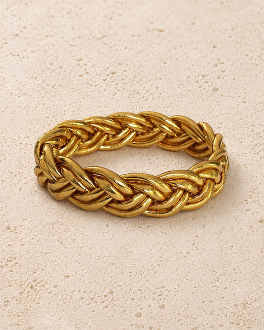 Jonc bouddhiste or tressé Bâan Kumlaï, bracelet Kumlai doré présenté seul sur fond minéral chaud