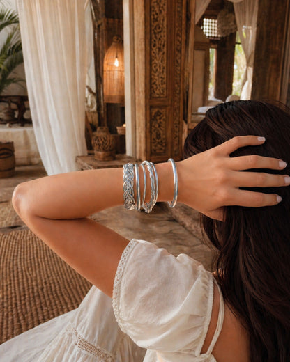 Main dans les cheveux avec plusieurs joncs bouddhistes argent Bâan Kumlaï, dont bracelets Kumlai torsadés, fins et tressés